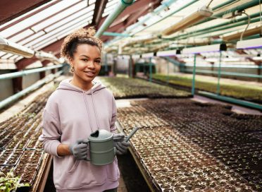 Happy young African-American farmer with watering-pot