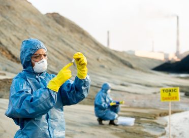 Researcher in protective coveralls looking at sample of toxic soil in hands