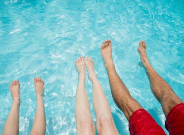 Family sitting on poolside and shaking their legs in pool water